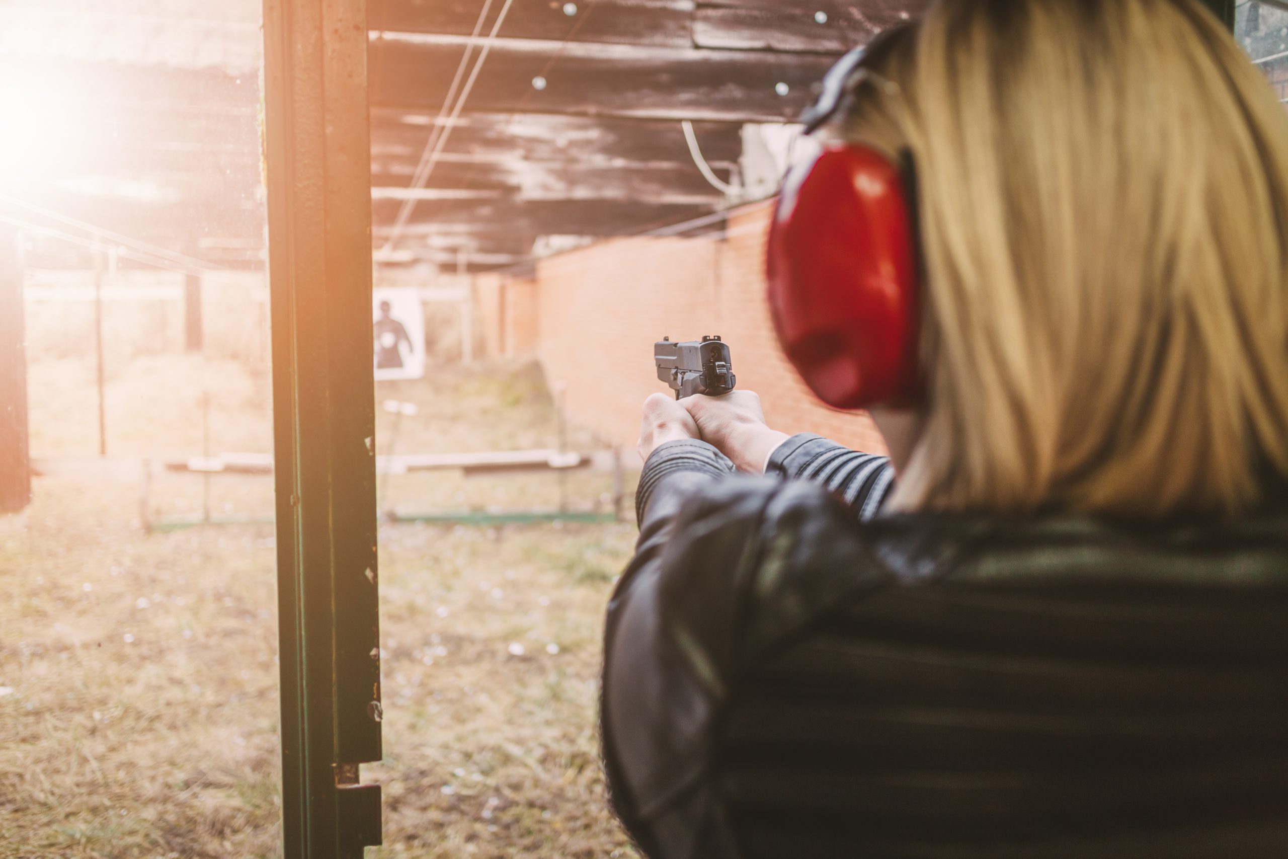 A person wearing ear protection while shooting a handgun at an outdoor range.